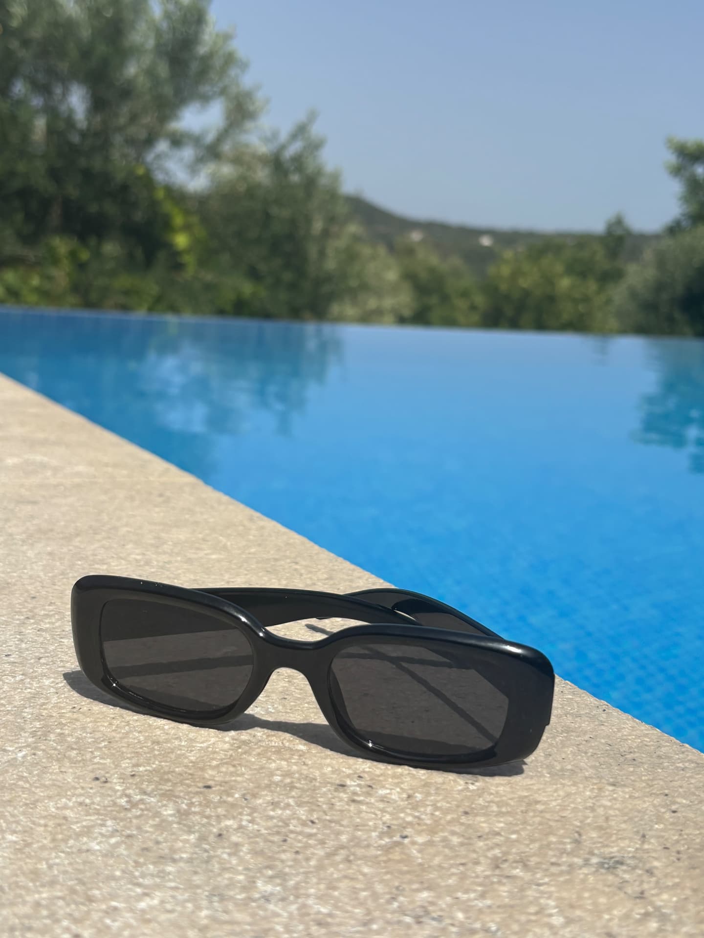 Obsidian No.1 sunglasses resting on stone beside an infinity pool